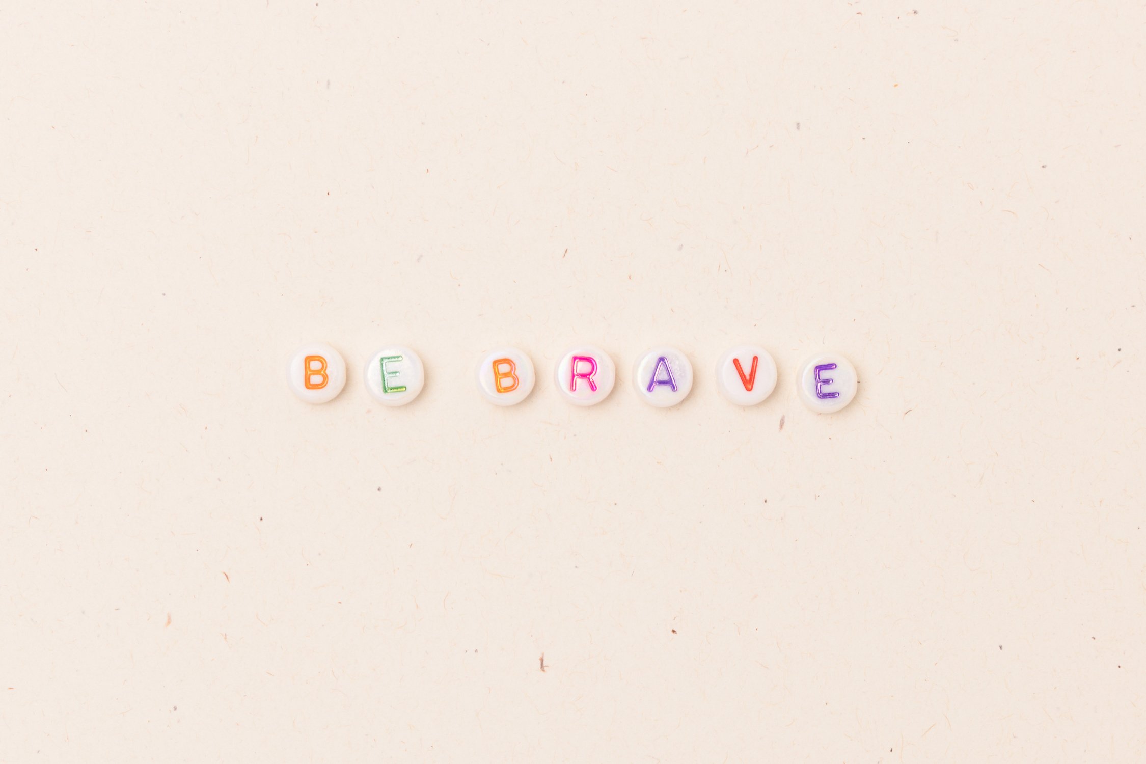 Be brave. Quote made of white round beads with multicolored letters.